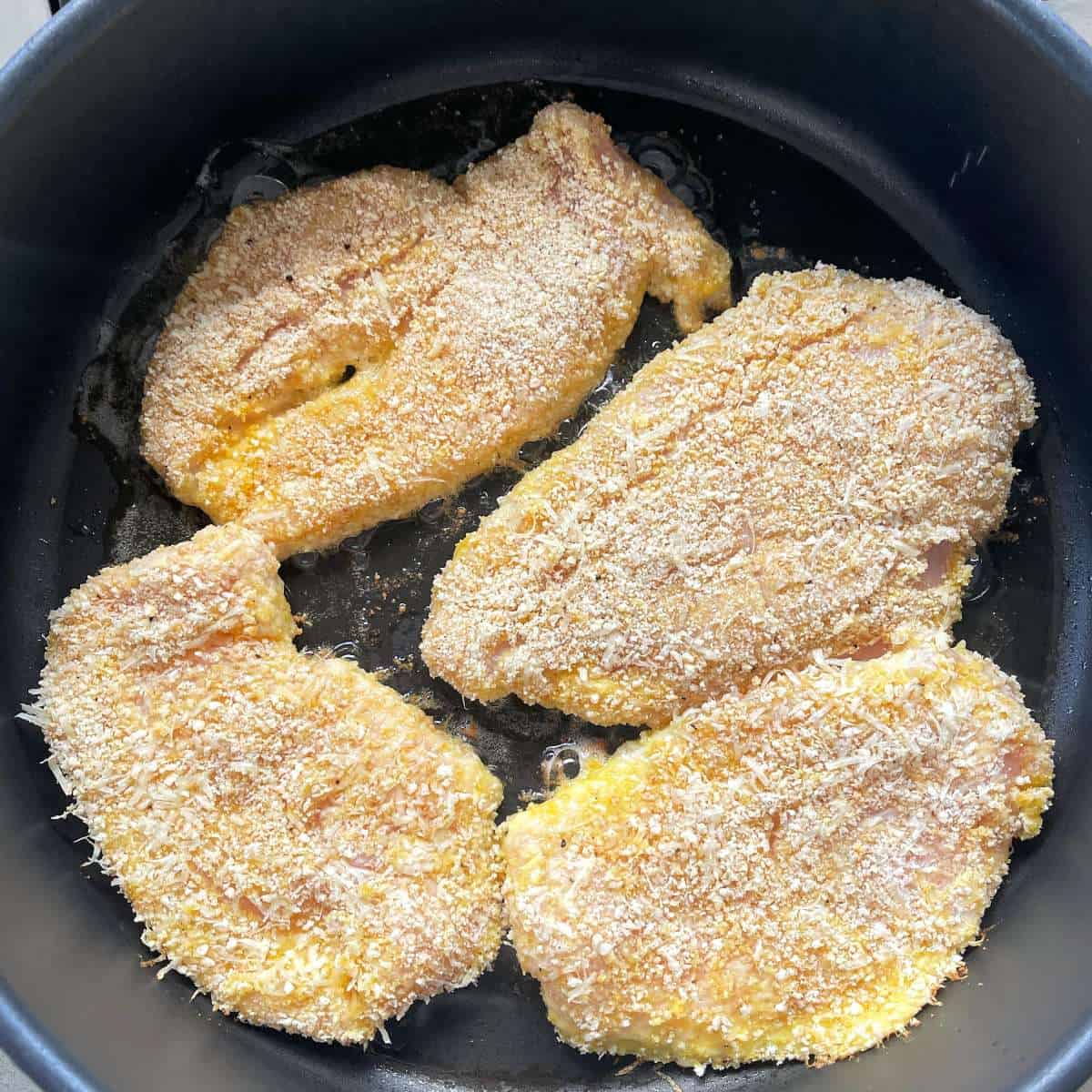Crumbed chicken breast frying in a frypan