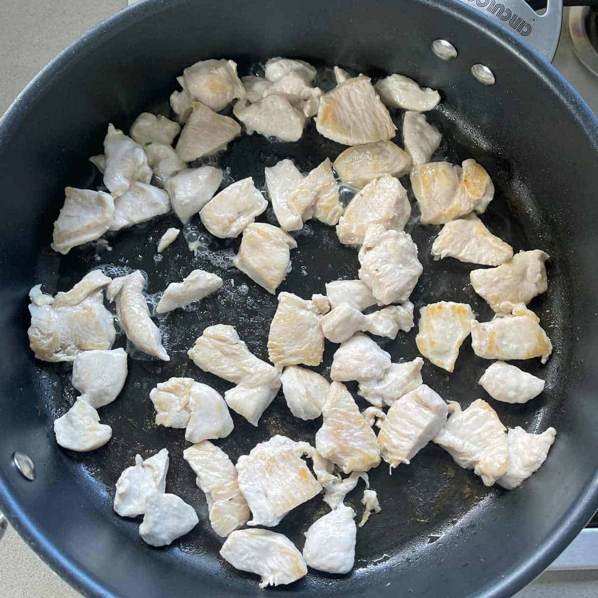 Cubed chicken breast frying in a frypan