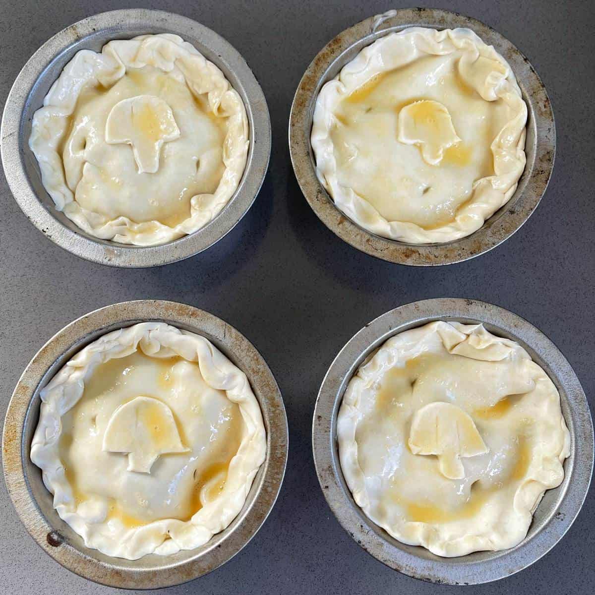 Four uncooked chicken and mushroom pies sitting on a grey bench