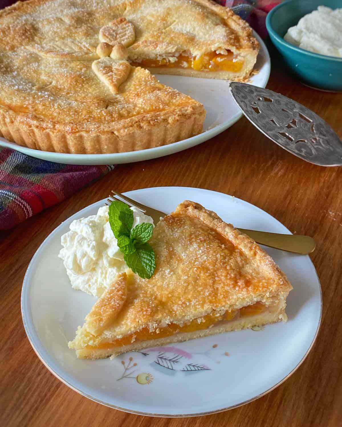 One slice of cooked apricot short crust pie on a white plate served with cream and a mint leaf