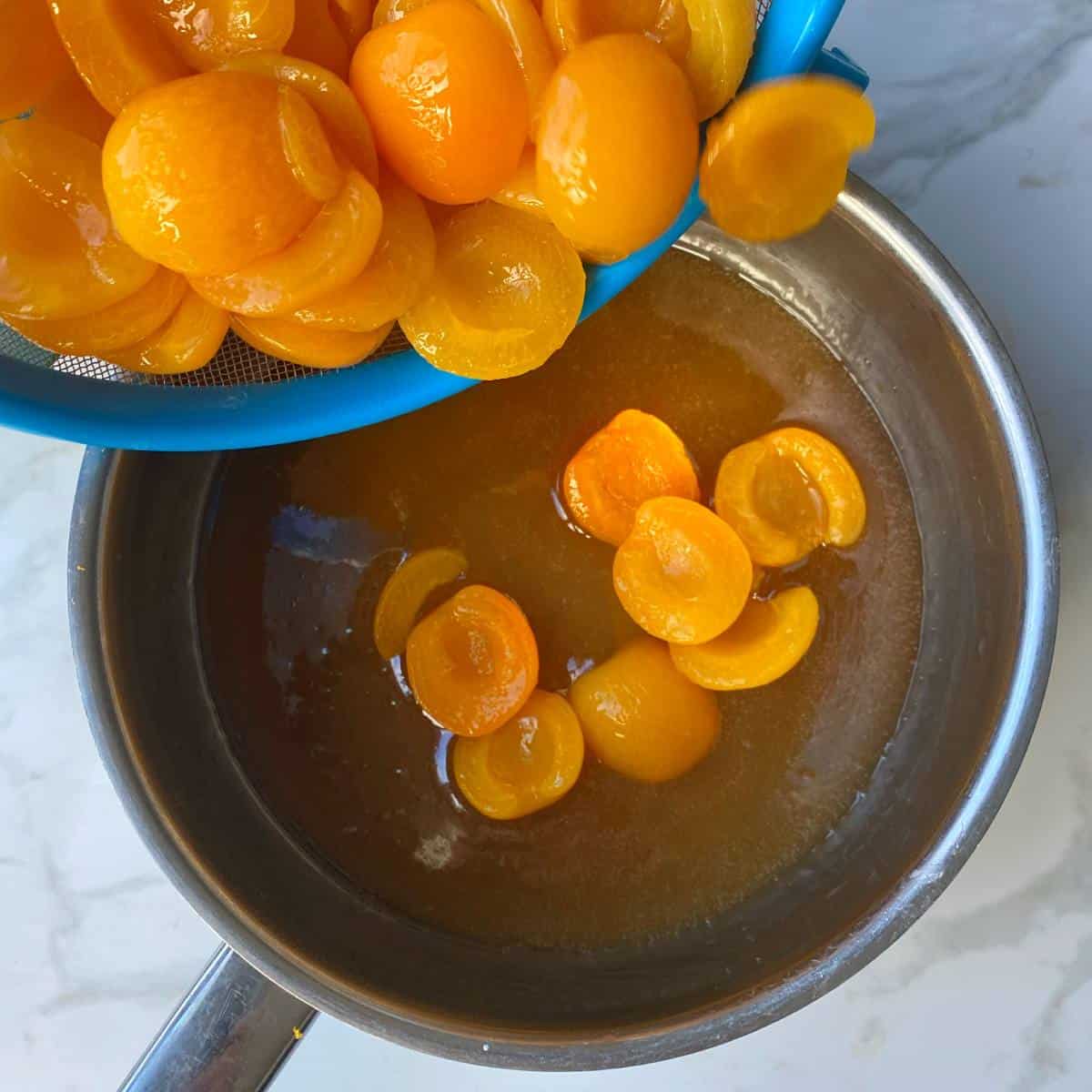 Drained apricots being poured into the sugar syrup