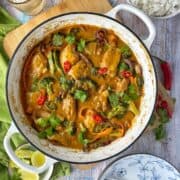 Cooked chicken satay yellow curry in a large white round oven dish sitting on a wooden chopping board