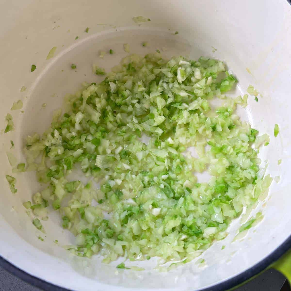 Diced onion and celery frying in a large round ceramic pot