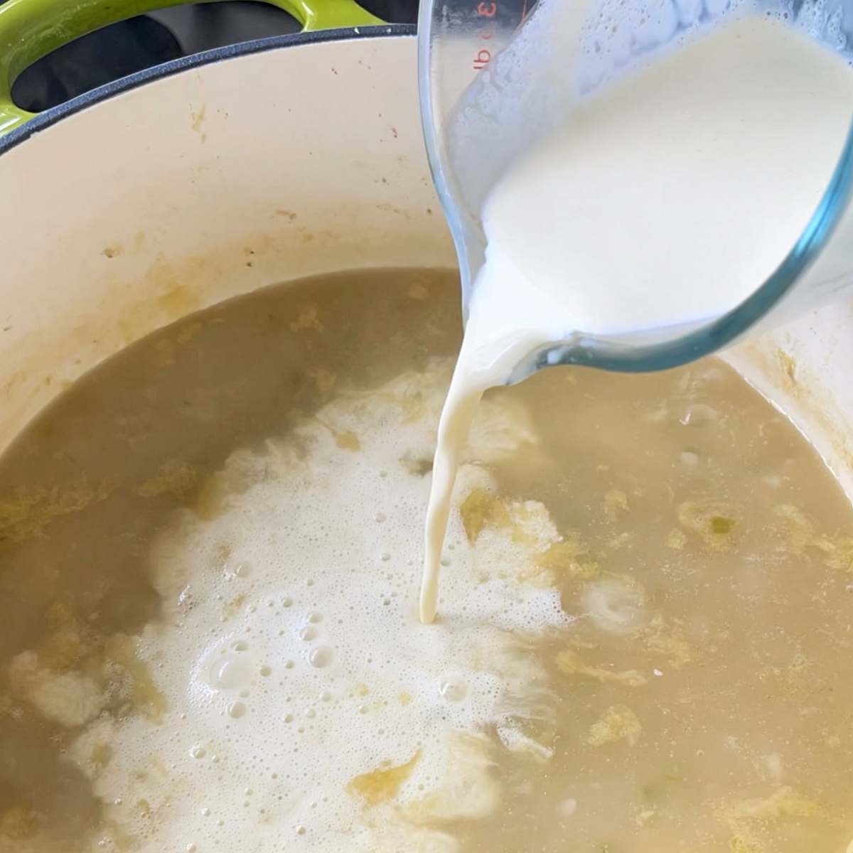 Cream being poured into the seafood chowder broth over a medium heat