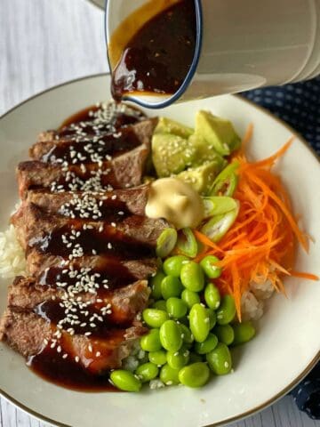 Teriyaki steak served in a white bowl with sauce being poured over the top