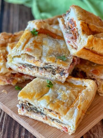 Pieces of bacon and egg pie stacked up on a wooden board.
