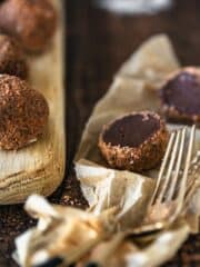 One Chocolate Bailey Truffle sliced in half showing the chocolate filling. Reminder truffles sitting on a wooden chopping board
