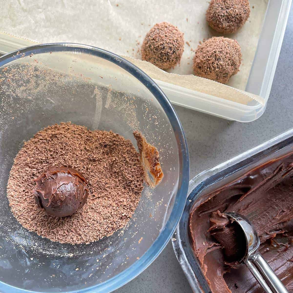 The chocolate bailey truffle mixture, shredded chocolate in a separate glass bowl with one truffle being rolled through it covering the outside of the truffle.