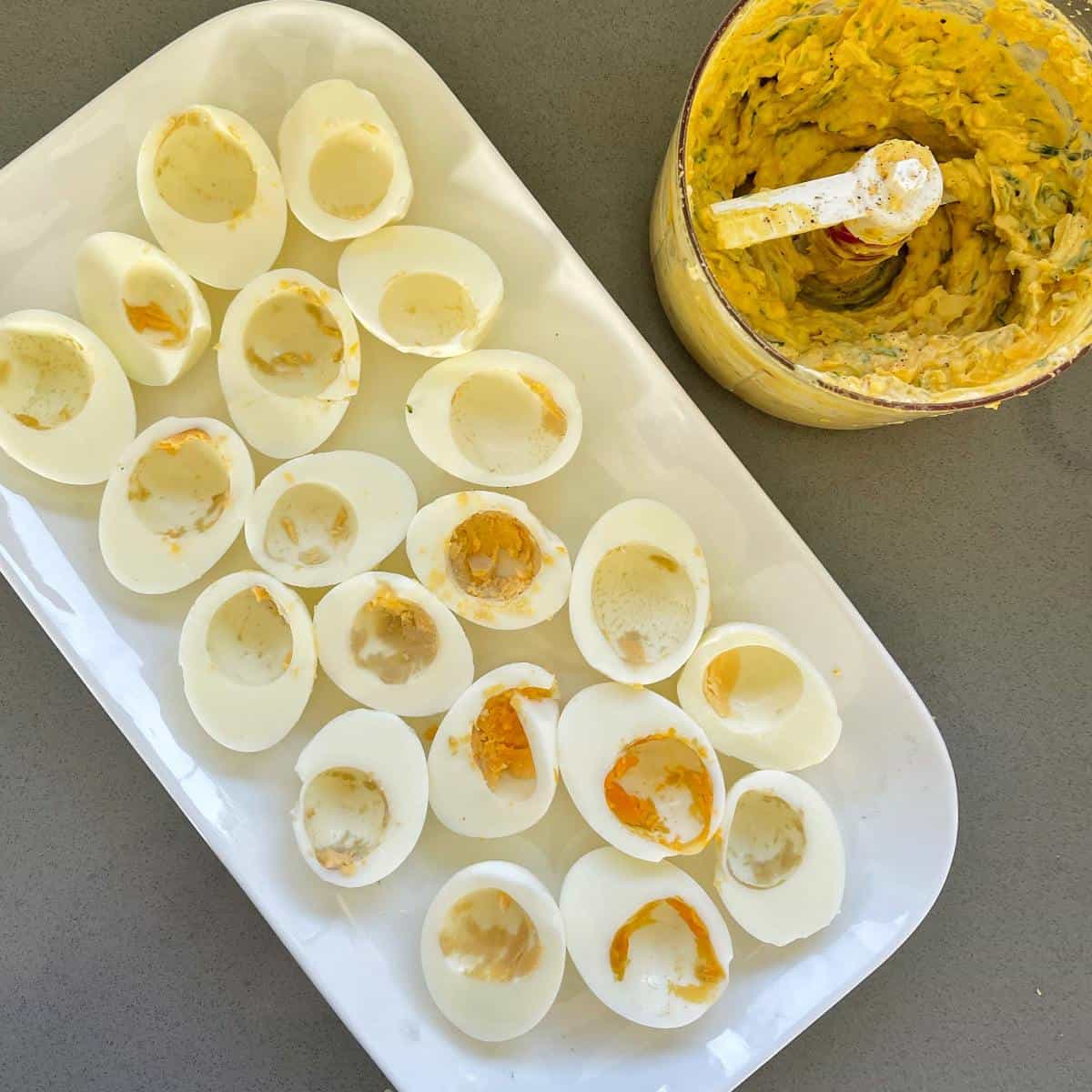 Boiled eggs cut in half with the yoke removed. The curried egg mixture in a small dish to the side.