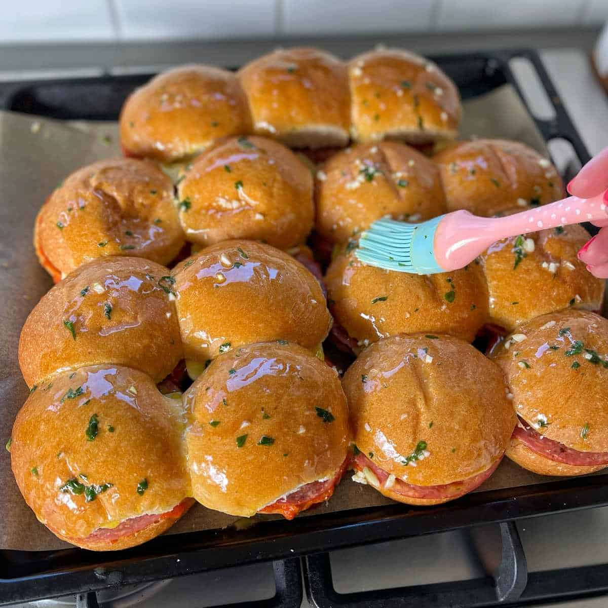 Assembled pepperoni sliders with a butter herb and garlic mix on top on a lined oven tray