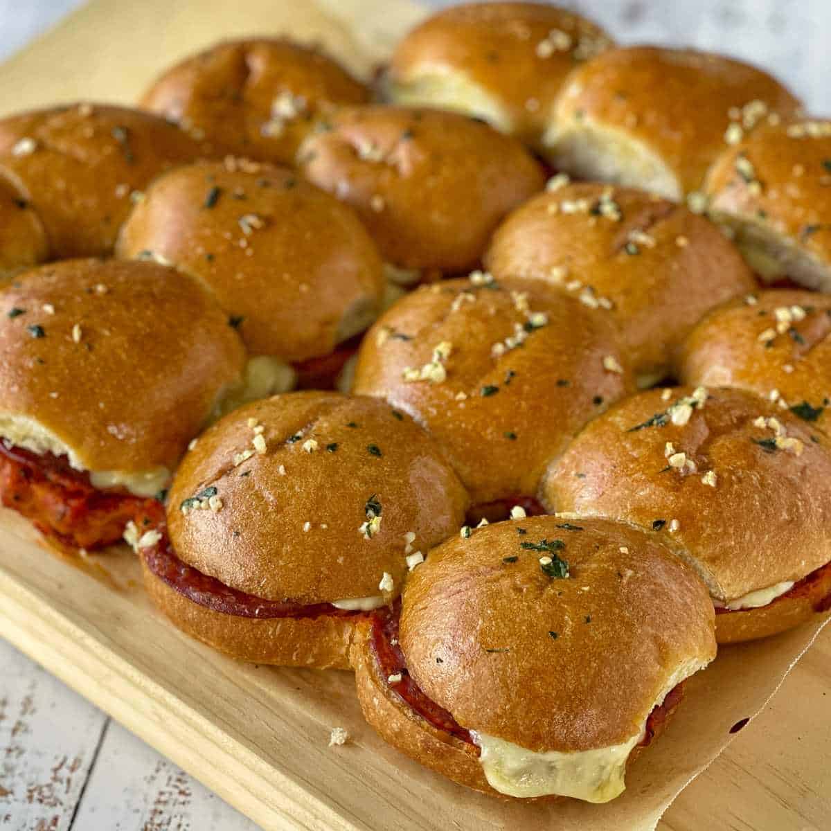 Cooked pepperoni sliders assembled on a wooden chopping board