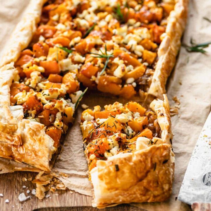Cooked pumpkin and feta tart with the corner sliced party removed, sitting on baking paper on a wooden chopping board.
