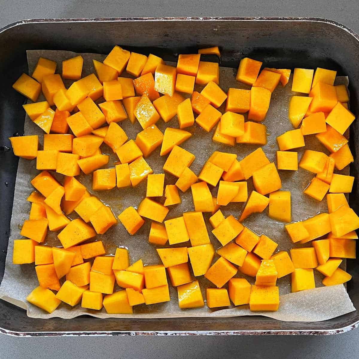 Cubed pumpkin pieces covered in mayple syrup in a lined roasting tray