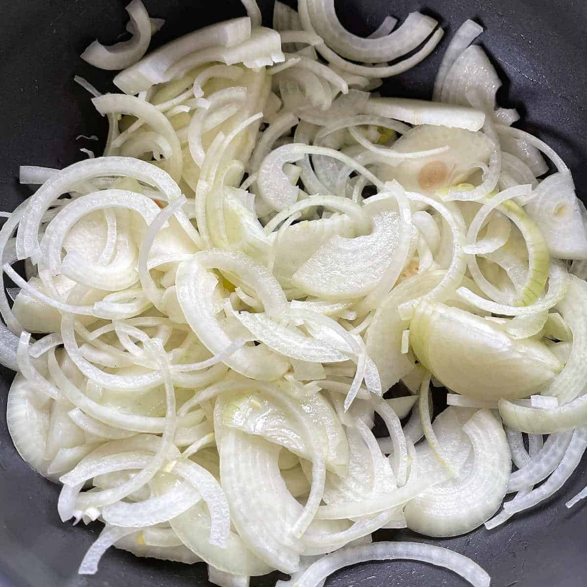Sliced onions in a fry pan with a splash of olive oil