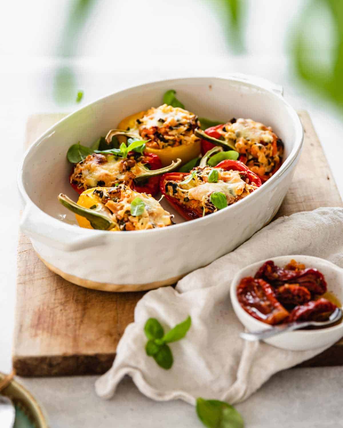 Cooked stuffed capsicums served in a white oval dish with basil leaves scattered on top