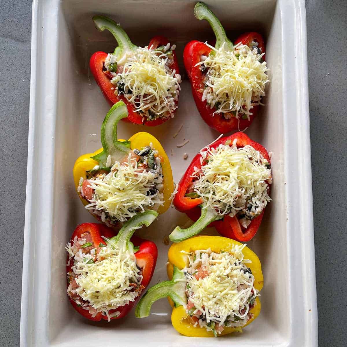 Six stuffed capsicums with grated cheese on top before they have been cooked