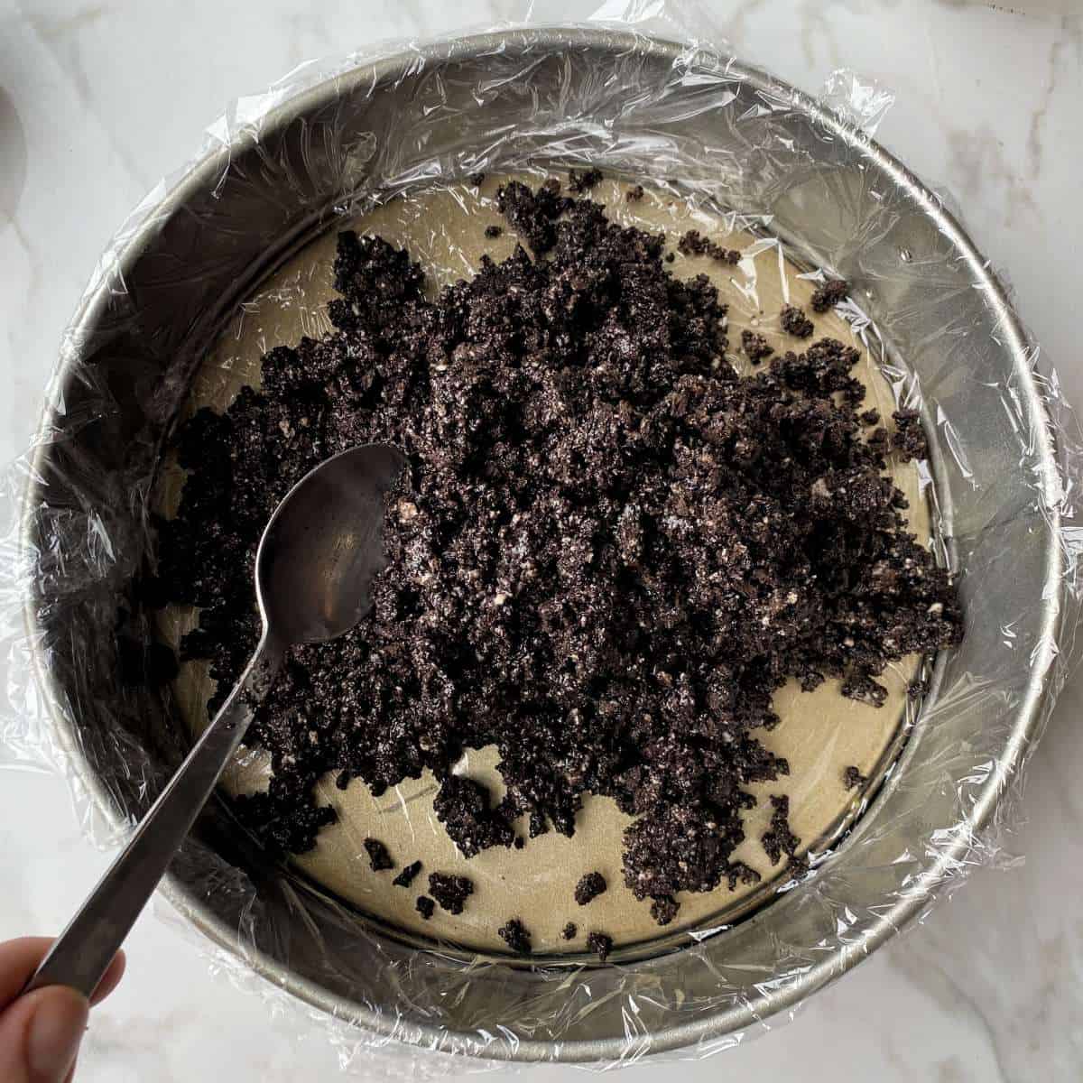 The oreo base for the top deck cheese cake being put into a lined cake tin