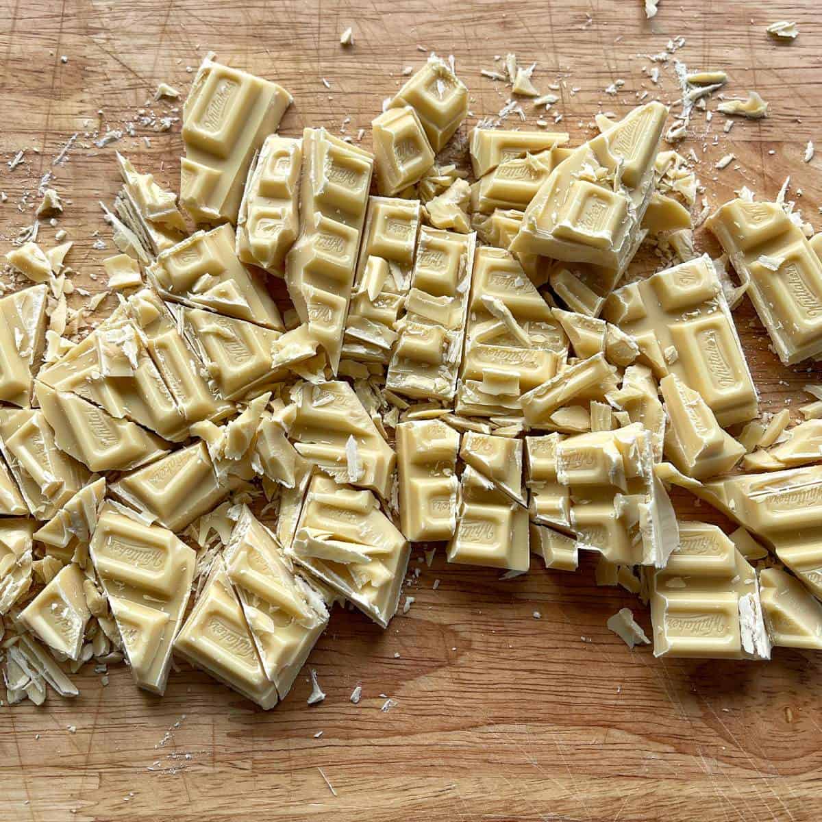 Broken pieces of white chocolate on a wooden chopping board