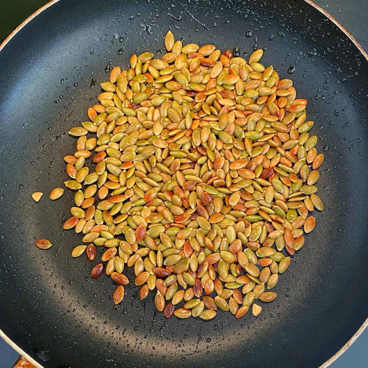 Pumpkin seeds toasting in a small frypan