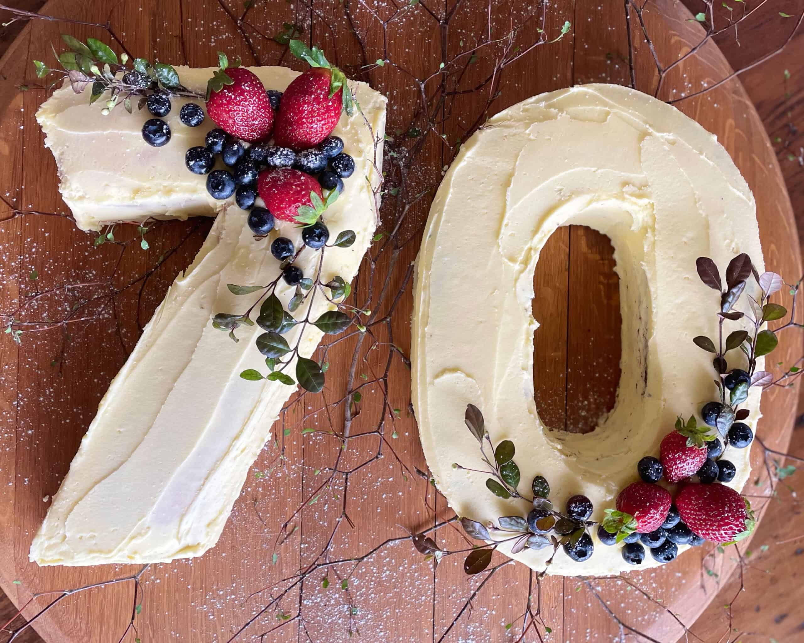 A 7 and 0 number cake with white icing and fruit on top.