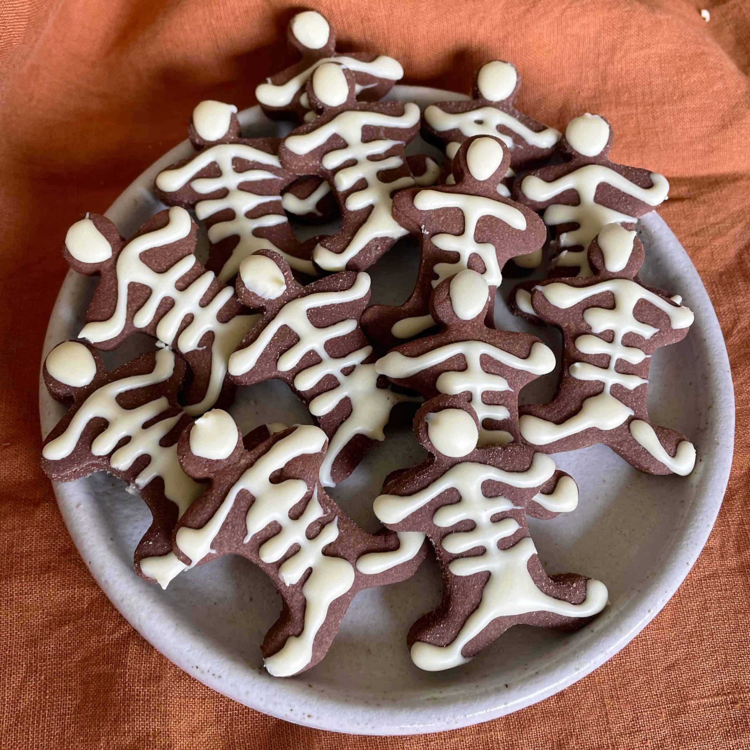 Small Skeleton Cookies on a small white plate on an orange tablecloth.