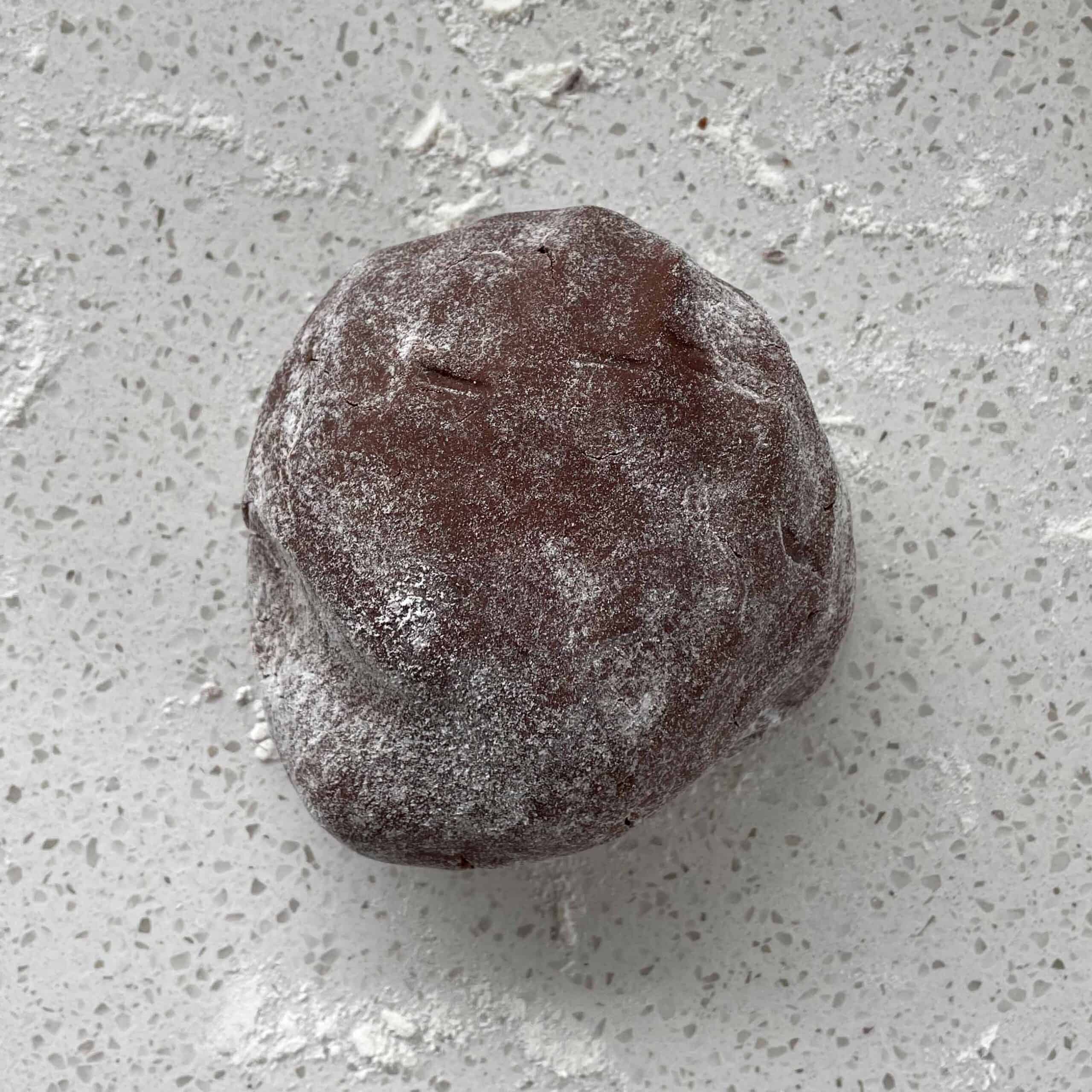 A ball of chocolate shortbread dough covered in flour on a white bench.