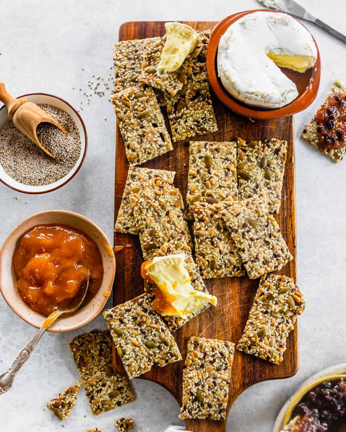 Cooked seeded crackers being served with cheese and chutney on a wooden platter