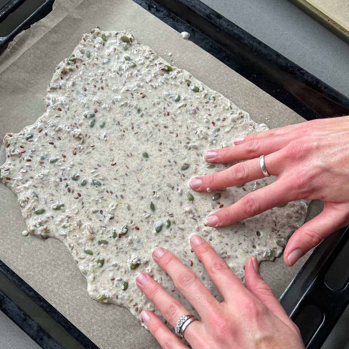 The seeded cracker mixture spread out on an oven tray lined with baking paper