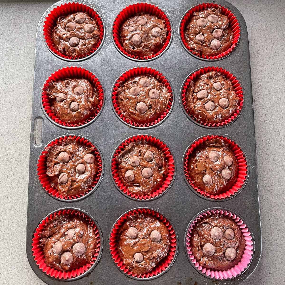 12 uncooked chocolate muffins sitting in the muffin tray on a grey bench top