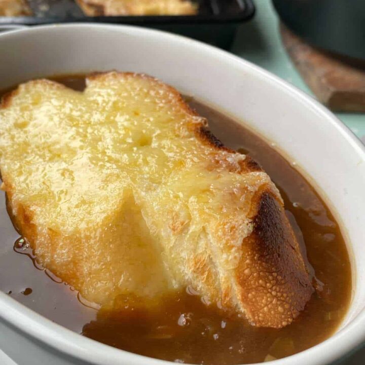 French onion soup with cheesy bread on top served in a small oven white soup bowl.