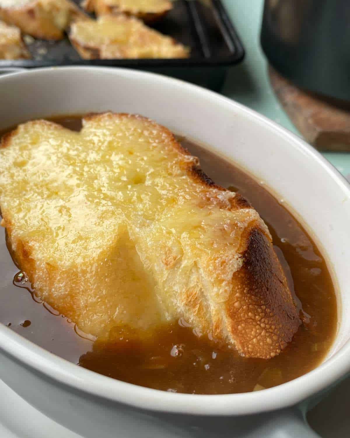 French onion soup with cheesy bread on top served in a small oven white soup bowl.