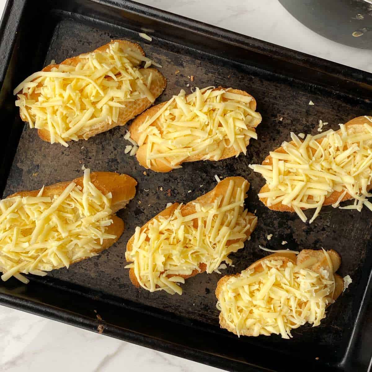 Slice of bread with grated cheese on top on a baking tray.