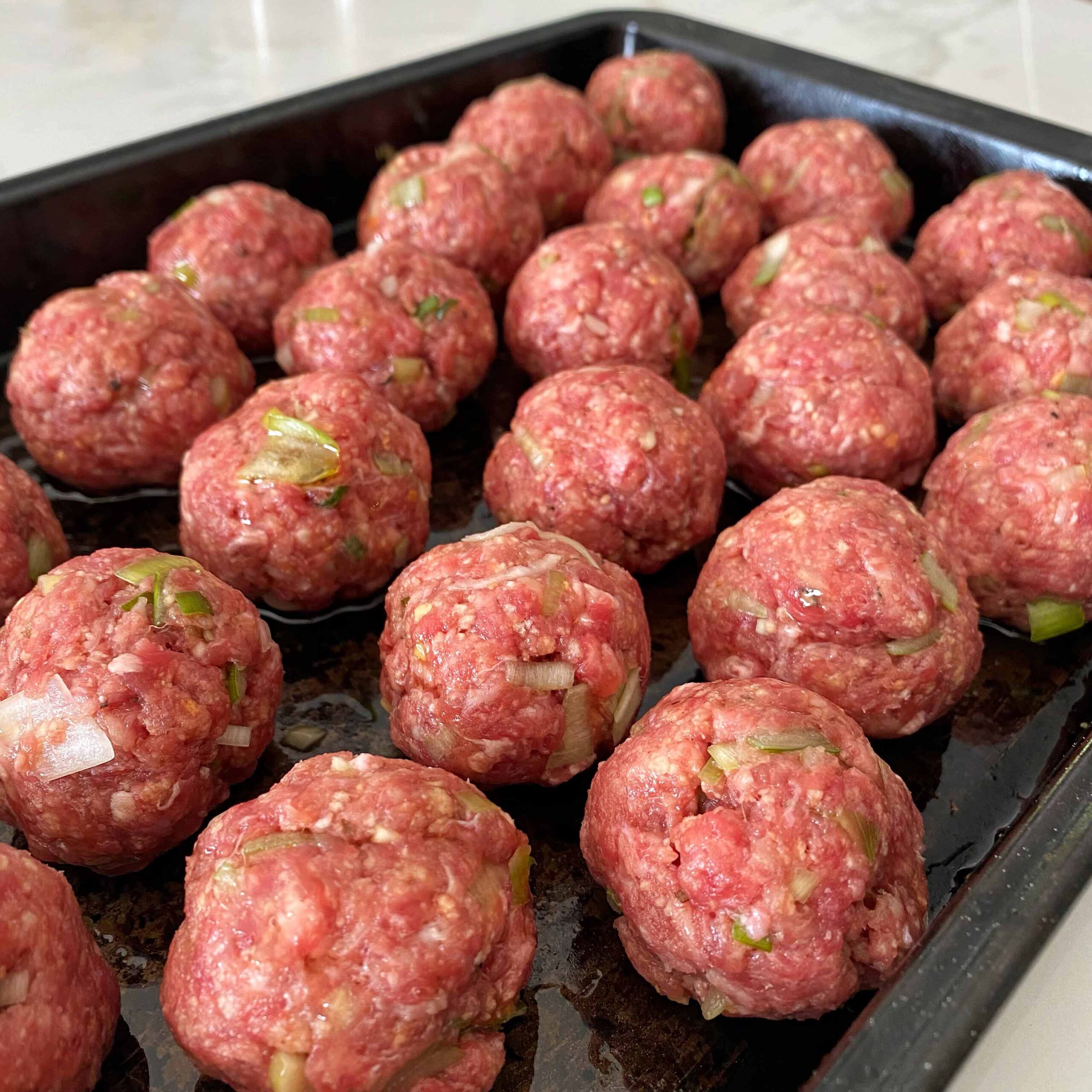 Rolled meatballs on a baking tray.