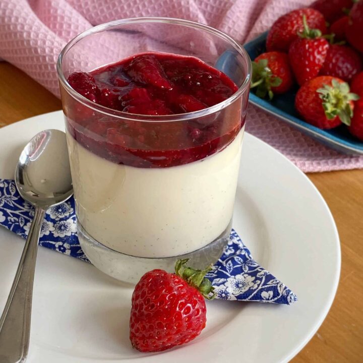 A strawberry Panna cotta in a glass on a white plate.