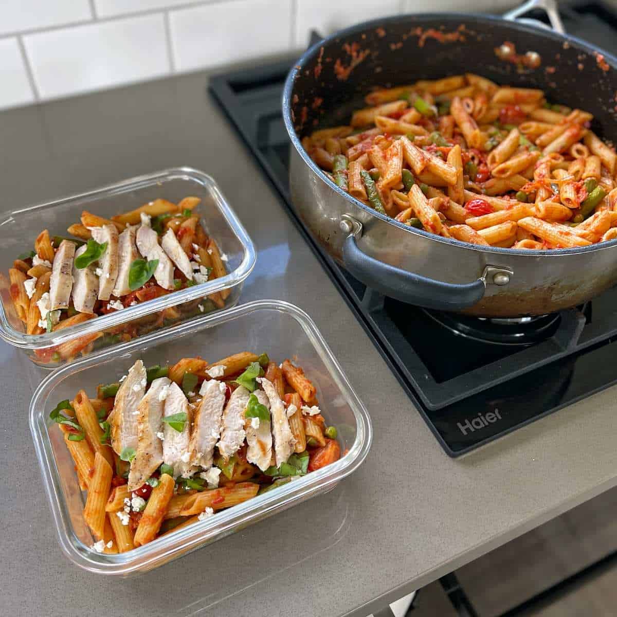 Chicken pasta cooking from a pan being distributed to reusable containers for lunch prep.