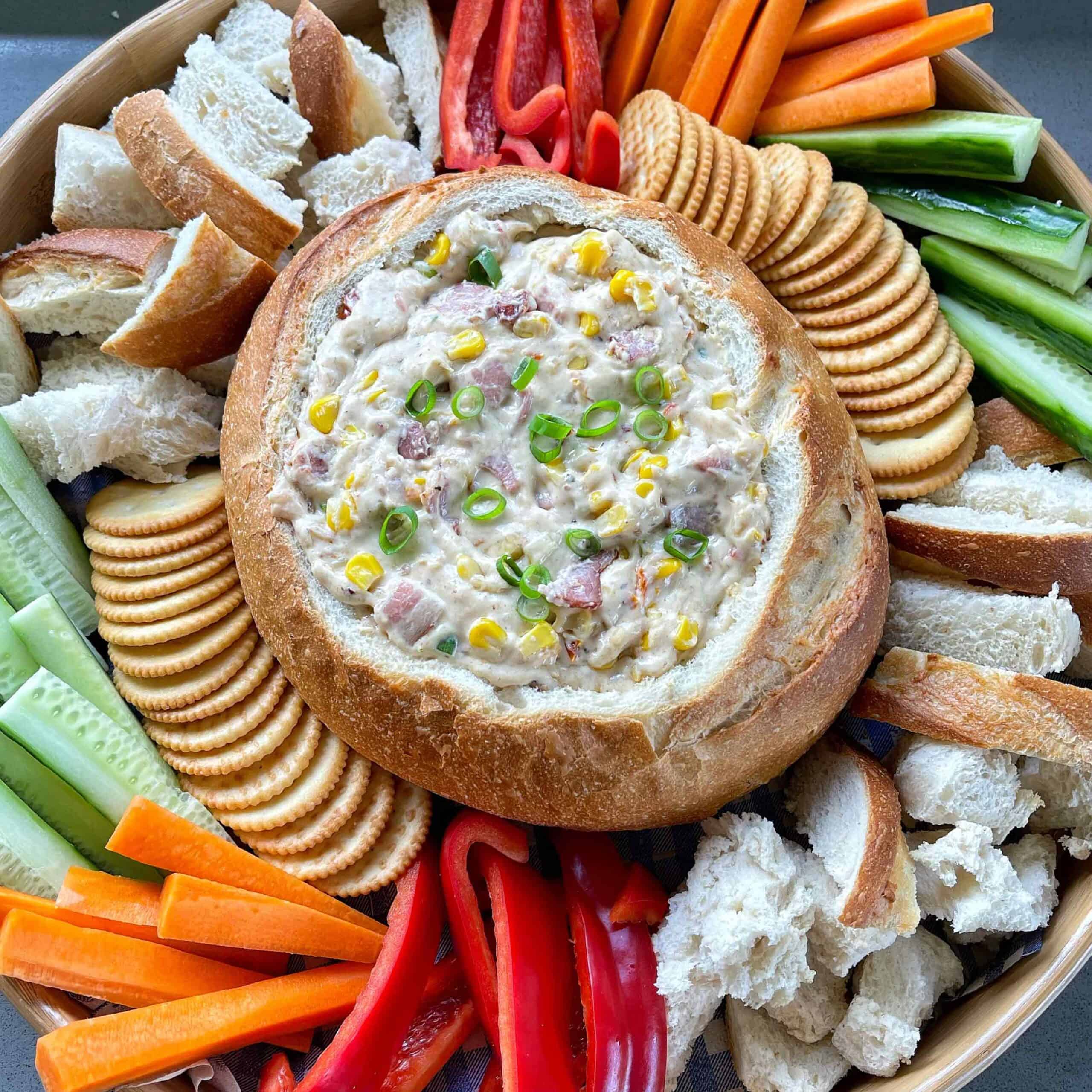 A Cowboy Cob Loaf served on a platter surrounded by vegetables, bread and crackers.