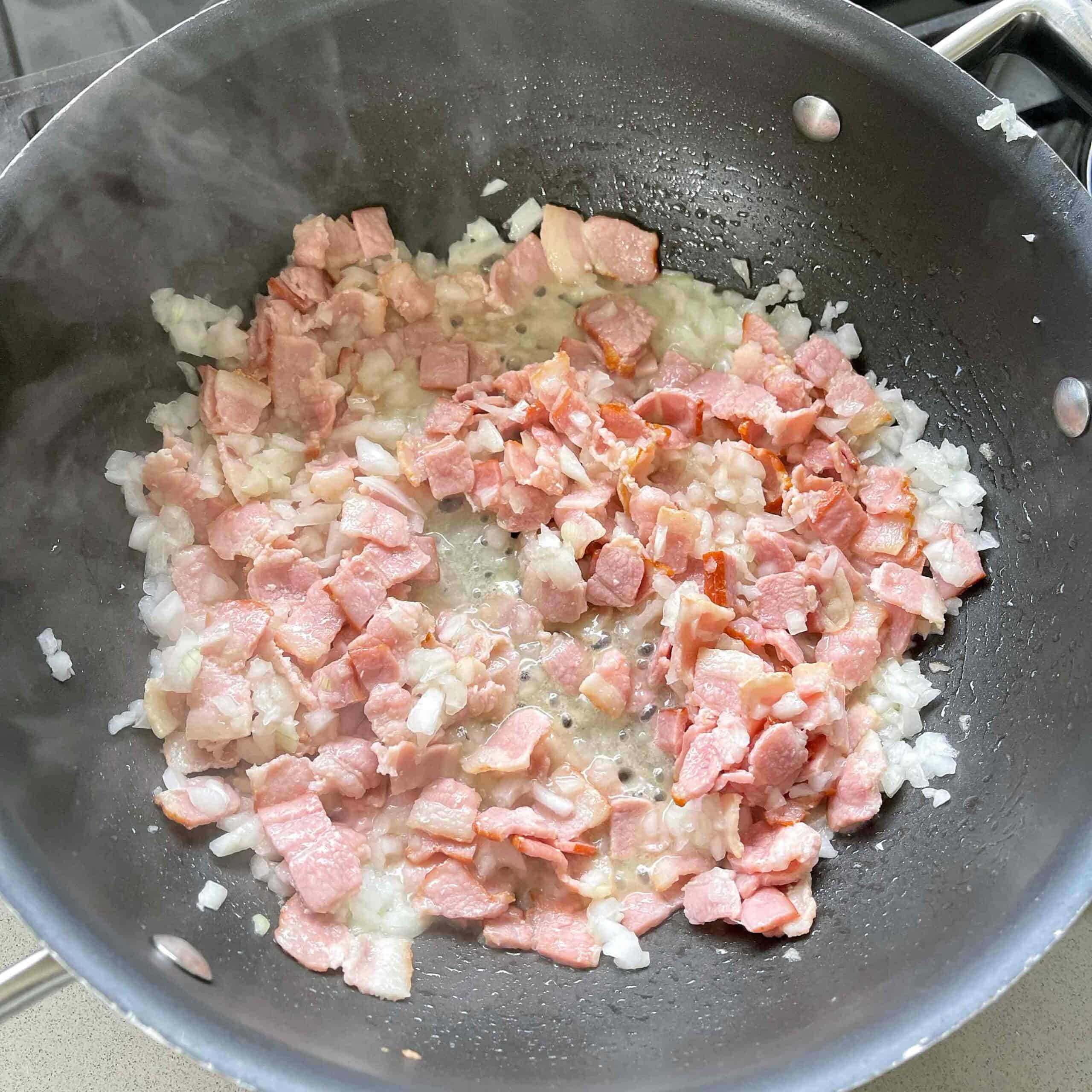 Bacon and onion frying in a large frying pan.