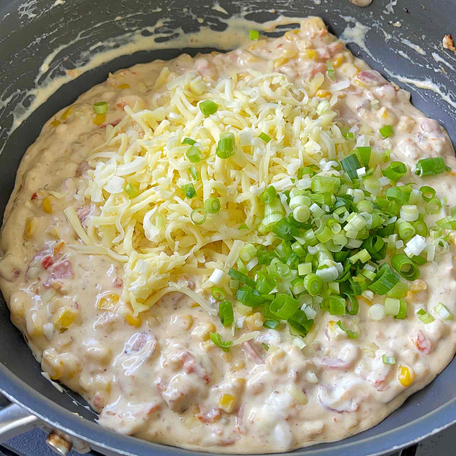 Creamy bacon and corn dip in a frying pan with mozzarella and spring onion added.