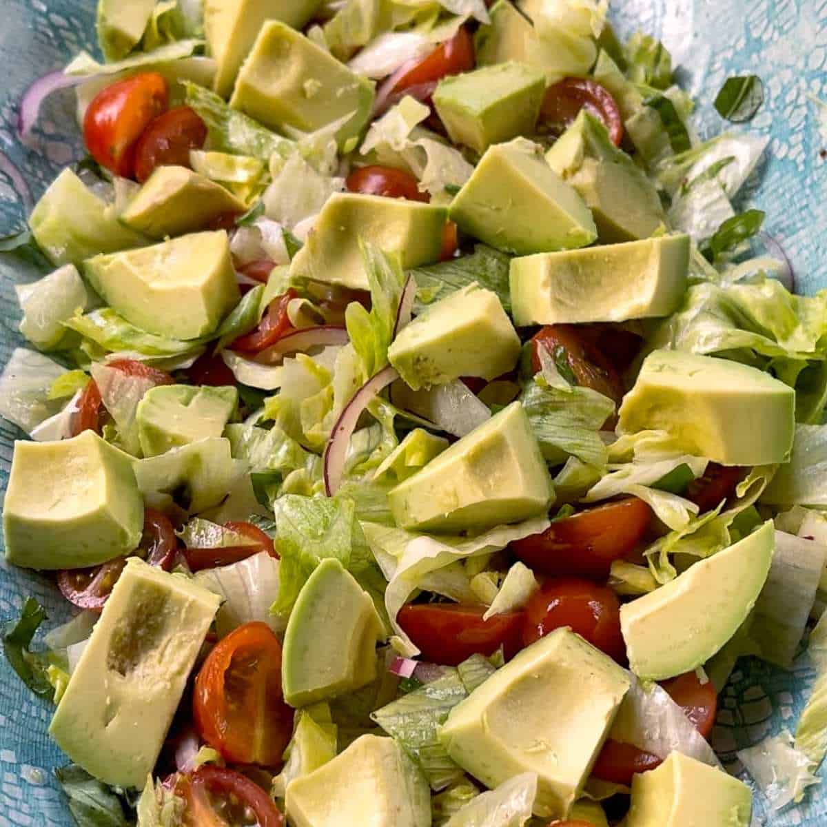 Lettuce, avocado, red onion and cherry tomatoes in a dish.