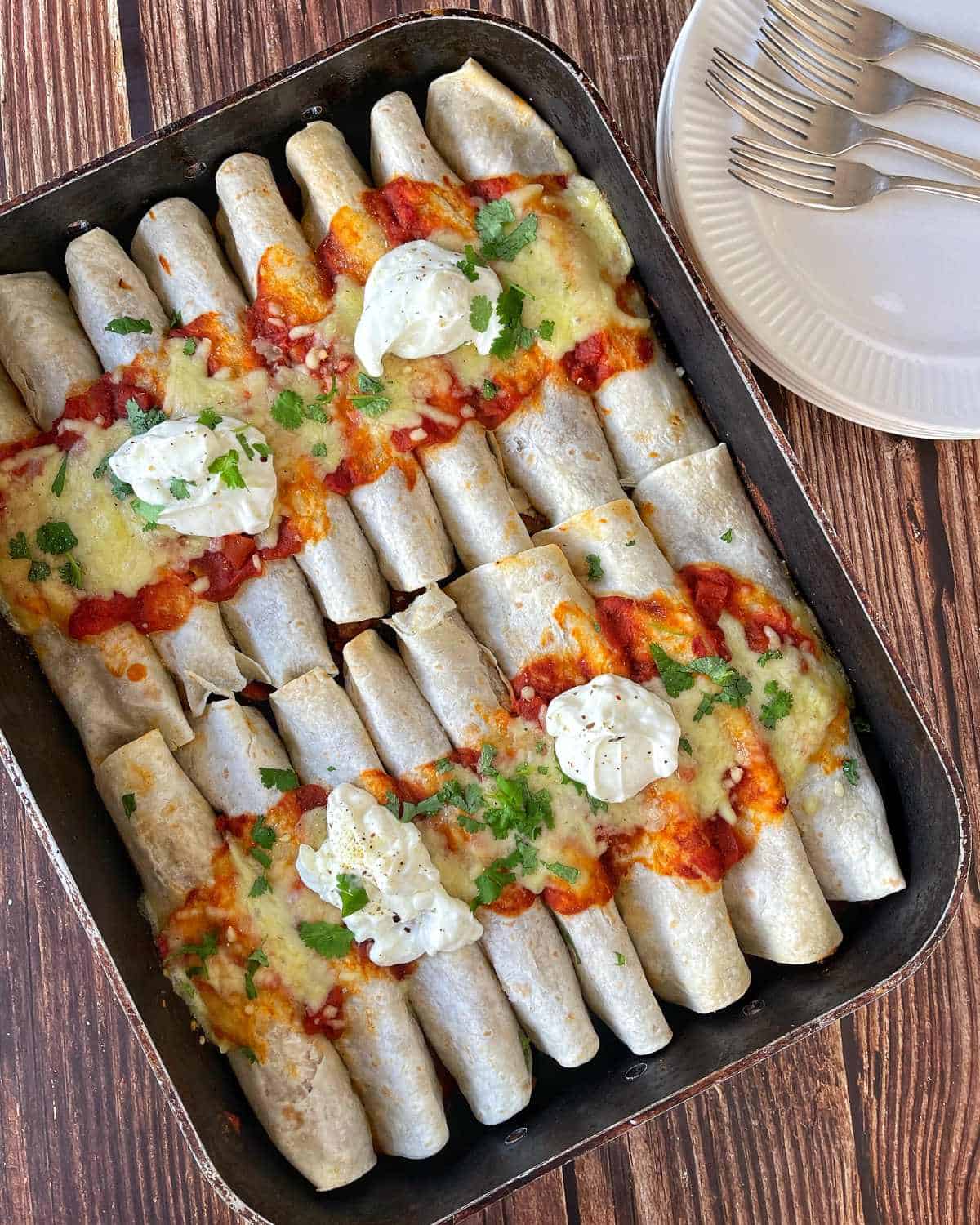 Cooked beef enchiladas served with sour cream and coriander