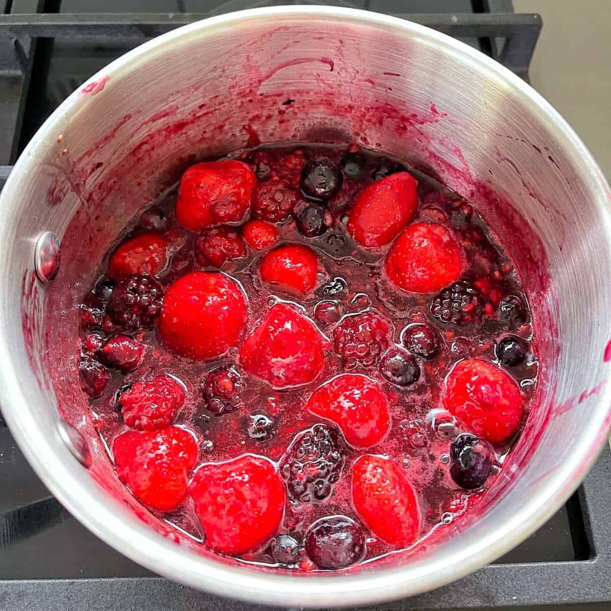 Berries simmering in a saucepan on the stovetop.