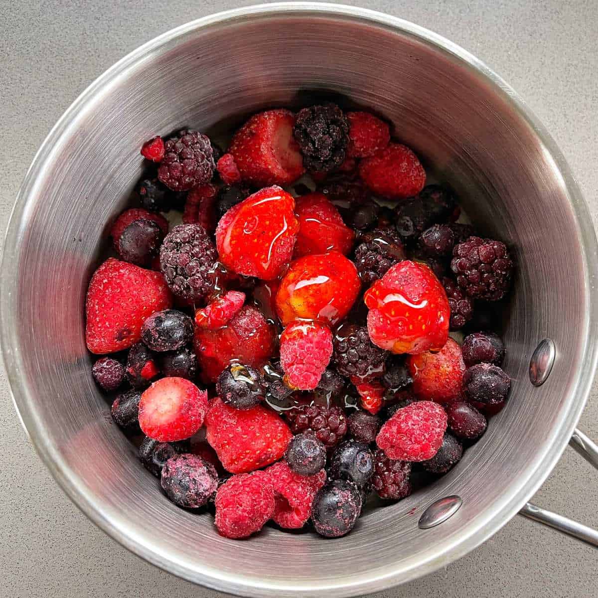 Frozen berries in a saucepan on a grey bench.