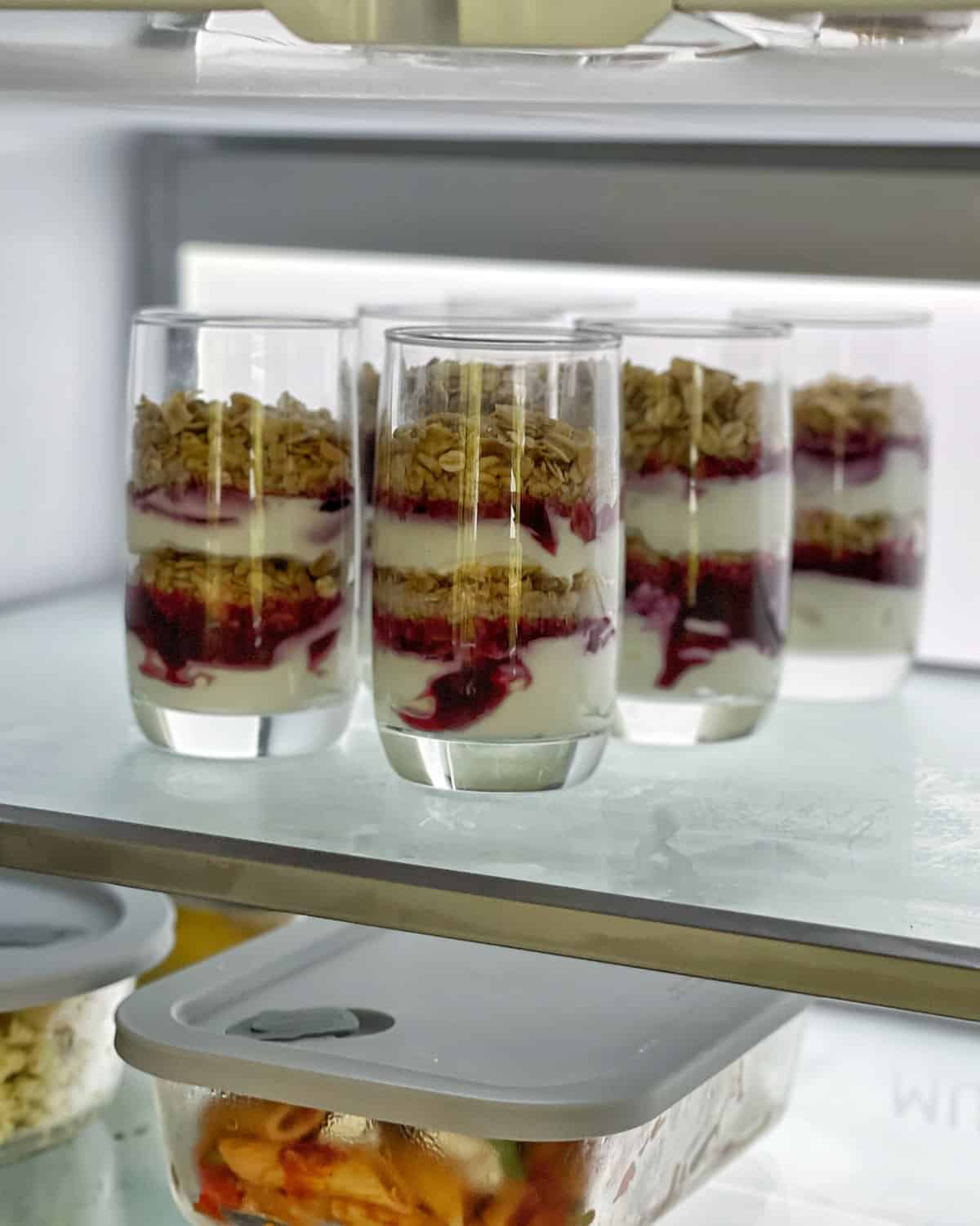 6 tall glasses layered with yoghurt, berry compote and toasted muesli in the fridge