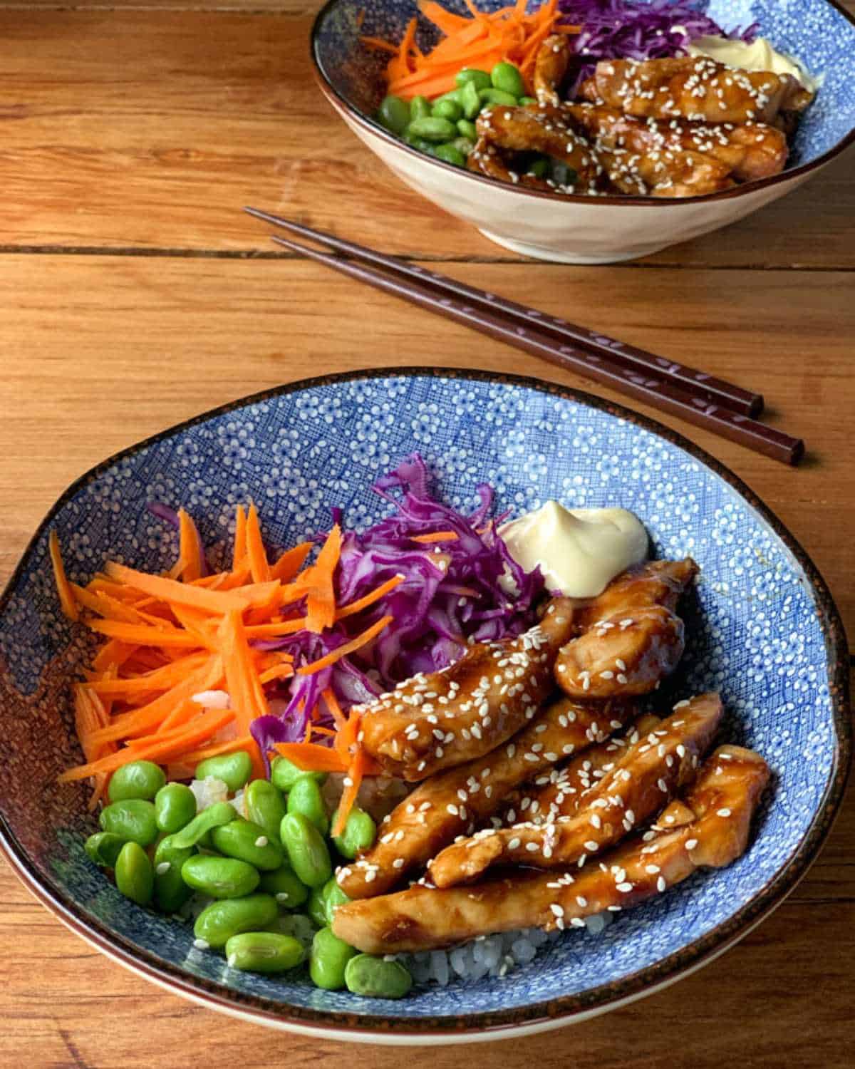 Two bowls of Teriyaki chicken sitting on a wooden table.