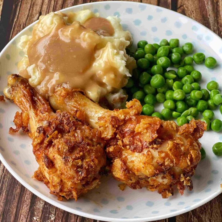 A plate of chicken, peas, mashed potato and gravy on a wooden table.