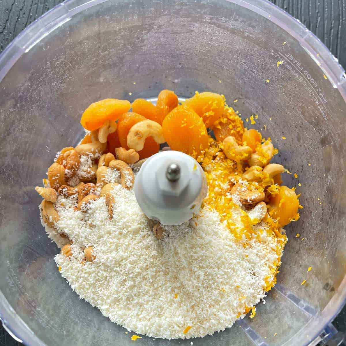 Coconut, lemon zest, honey, cashew nuts and apricots in a small food blender ready to be blended to make Apricot Bliss Balls.