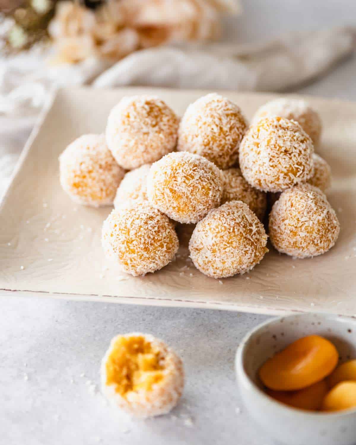Apricot Bliss Balls stacked on top of one another, served on a off white square plate.