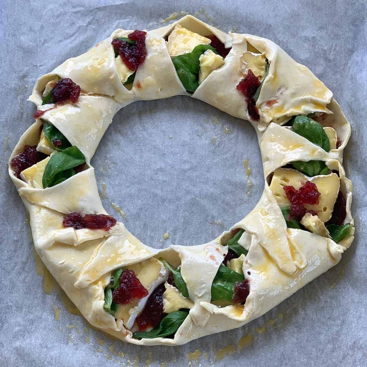 Uncooked but assembled brie and cranberry wreath sitting on a line baking try