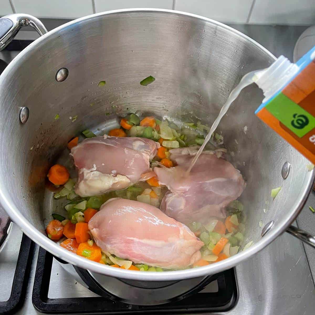 Stock being poured into a large pot containing chicken and vegetables.