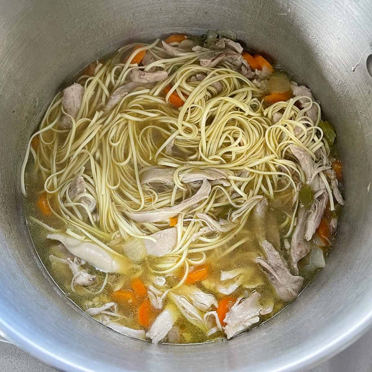 Chicken noodle soup cooking in a large pot.